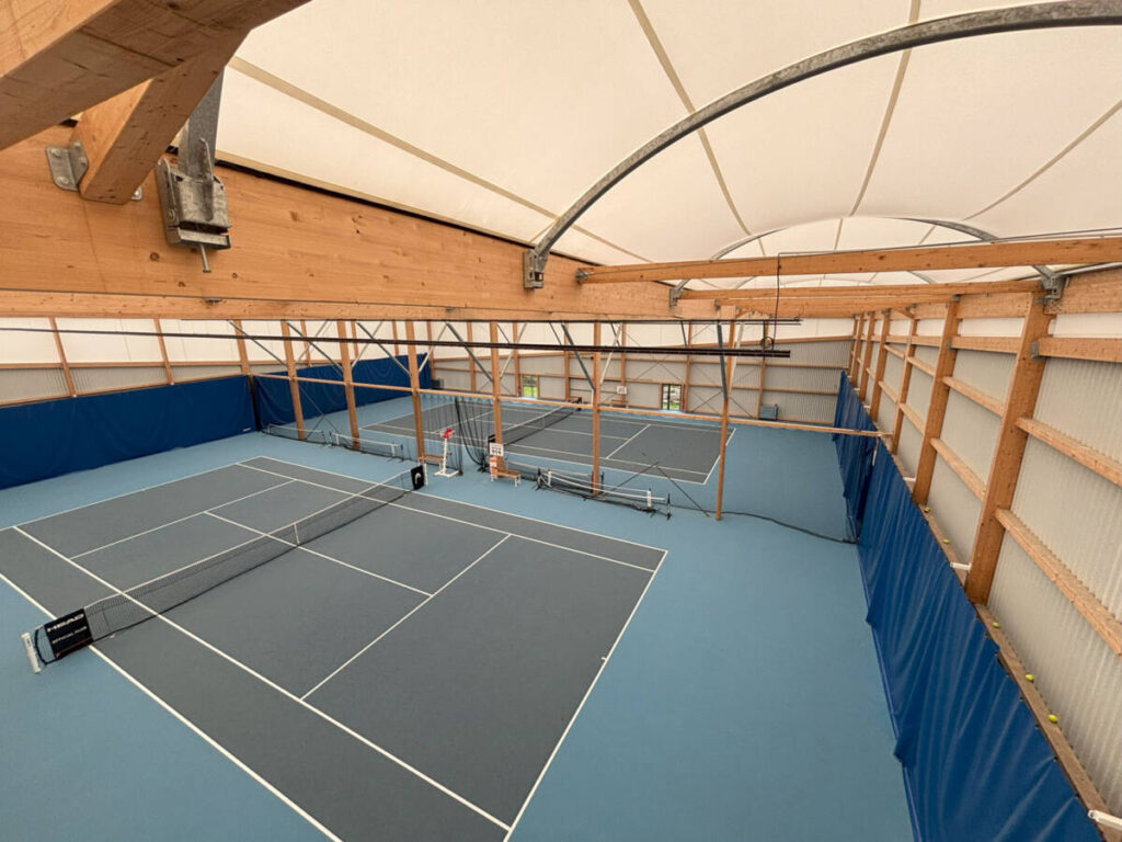 Construction d’un tennis couvert de 1400 m² : charpente bois lamellé-collé, membrane textile et sol sportif performant.