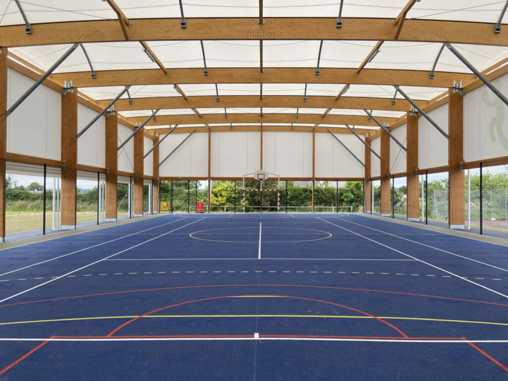 Découvrez le nouveau préau multisport de 908 m² à Quettreville-sur-Sienne, alliant membrane textile, charpente mixte et équipements modernes.
