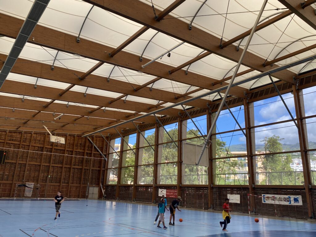 Halle sportive à Joinville (974) : structure bois lamellé-collé et membrane textile, conçue pour résister au climat tropical de La Réunion.