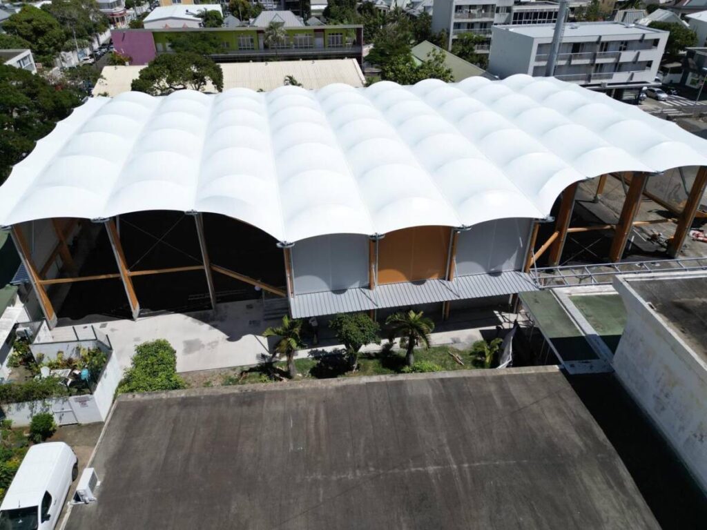 Halle sportive à Joinville (974) : structure bois lamellé-collé et membrane textile, conçue pour résister au climat tropical de La Réunion.